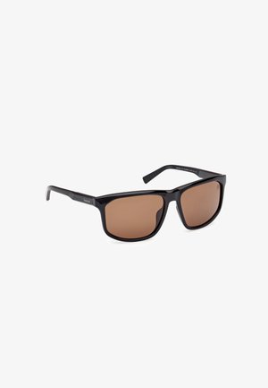 Occhiali da sole con montatura nera e lenti color marrone. Forma quadrata con una superficie liscia e dettagli in metallo sul lato.