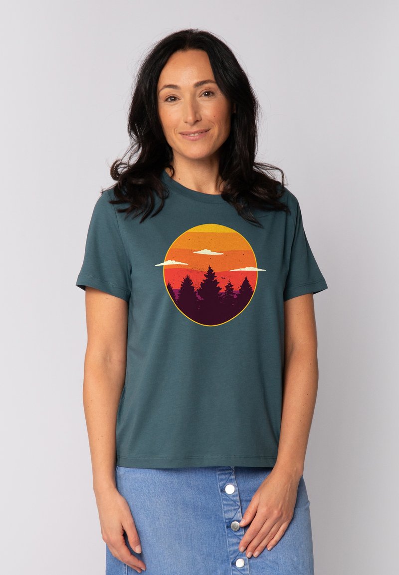 Teal katoenen t-shirt met korte mouwen, voorzien van een cirkelvormige grafiek van een zonsondergang en dennenbomen in oranje, paarse en gele tinten.