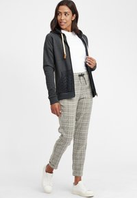 Mörkgrå zip-up hoodie med en kabelstickad ficka, ljus krämfärgade dragskor och en vit t-shirt under. Matchad med rutiga byxor och vita sneakers.