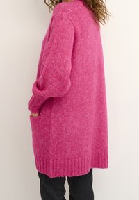 Cardigan rosa lavorato a maglia con una vestibilità morbida, spalle scese, tasche laterali e orli a coste. La texture morbida ne esalta l'aspetto accogliente.