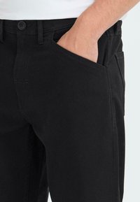 Zwarte denim broek met een rechte snit, voorzien van een voorzak en een knoopsluiting, textuurstof en een minimalistisch ontwerp.