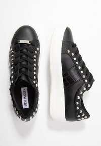 Mustat lenkkarit, joissa on teksturoitu krokotiilikuosi, hopeiset niittikoristeet sivuilla ja valkoinen pohja. Nauhoilla varustettu malli, jossa on sileä viimeistely.