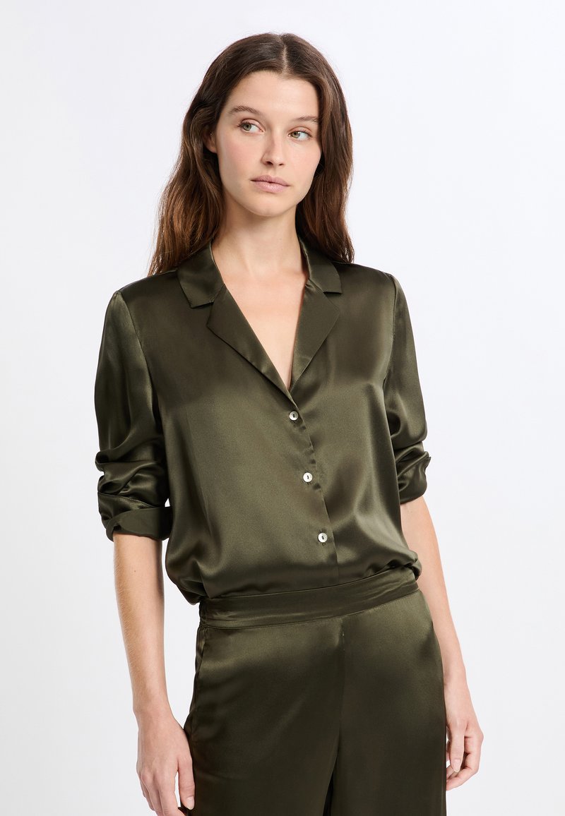 Blusa de satén verde oliva con cuello, cierre frontal con botones y mangas remangadas. Textura suave con un corte holgado y un ligero brillo.
