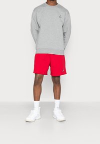 Felpa grigia con collo rotondo e piccolo logo, abbinata a pantaloncini rossi. Scarpe da ginnastica bianche e calzini completano il look.