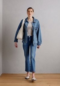 Jeansjakke med avslappet passform, hvit ribbet topp, blå utsvungne jeans, og hvite slip-on sko, supplert med en strukturert beige veske.
