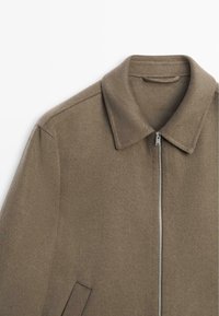 Bruine jas van een wollen mix met een rits aan de voorkant, klassieke kraag en schuine zijzakken. Zachte textuur, gestructureerde schouders en strakke lijnen.