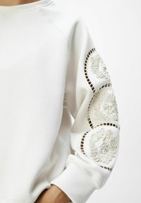 Witte sweatshirt met een ronde, textuurachtige bloemenontwerp op de mouwen en uitsnijdingen, met een relaxte pasvorm en geribbelde manchetten.