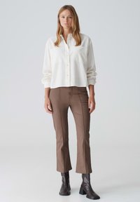 White button-up shirt with long sleeves paired with brown fitted pants. The outfit is complemented by black ankle boots.