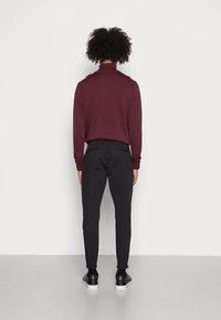 Suéter burdeos de manga larga, pantalones ajustados negros y zapatillas negras con suelas blancas. Diseño simple sin patrones o acentos notables.