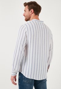 Camisa de manga larga de tejido ligero con rayas azules, con cuello mao y puños con botón, combinada con jeans azules.