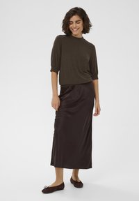 Brown knitted short-sleeve top paired with a long, sleek, dark brown satin skirt. Model wears dark brown flats. Smooth textures throughout.