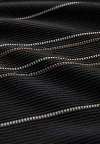 Schwarzer Stoff mit einem strukturierten Rippenmuster, das horizontale Linien dünner weißer und beiger Streifen aufweist. Weiche, wellenartige Falten sind sichtbar.