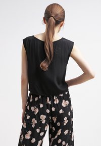 Top negro sin mangas con una textura suave y escote redondo, combinado con pantalones negros con un estampado floral en suaves tonos de rosa.