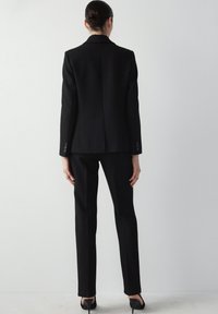 Černý oblek na míru s dobře padnoucím sakem s klopovým límcem a odpovídajícími slim-fit kalhotami, obojí vyrobené z hladké tkaniny.