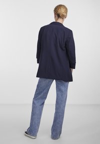 Námořnický blazer se strukturovanými rameny, dlouhými rukávy a přiléhavým střihem, doplněný světle modrými širokými džínami a černými teniskami.