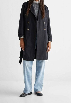 Cappotto trench doppio petto navy con bottoni dorati, abbinato a jeans a gamba larga blu chiaro e scarpe slip-on nere. Tessuto misto cotone.
