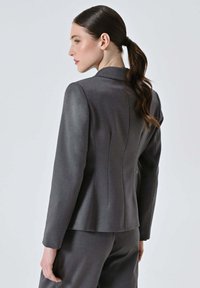 Blazer grigio sartoriale in tessuto liscio, caratterizzato da una silhouette aderente, colletto con rever e dettagli a cucitura. Progettato con maniche lunghe.
