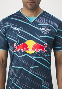 Puma futballmez sötétkék és türkiz színben, átlós csíkokkal, v-alakú nyakkal, az RB Leipzig logóval és sárga-piros Red Bull grafikával.