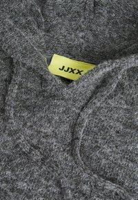 Maglione grigio con texture realizzato in tessuto morbido. Presenta un'etichetta gialla prominente con "JJXX" in testo nero vicino al colletto.
