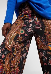 Zwarte broek met een patroon van complexe paisley- en bloemontwerpen in rood, oranje, groen en blauw, met een losse, wijde pasvorm.