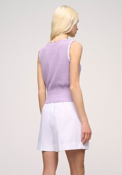 Fialový bezramínkový pletený top s texturovaným vzorem a žebrovaným lemem, v kombinaci s bílými přiléhavými šortkami s hladkým povrchem a ohnutými manžetami.