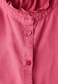 Camicia rosa con colletto arricciato e una fila di cinque bottoni rosa sul davanti, realizzata in un tessuto morbido.