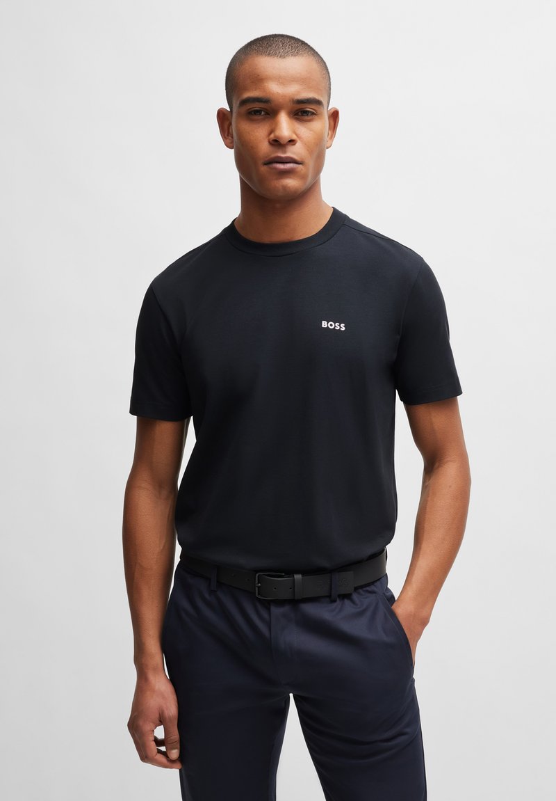 Svart t-shirt med rund halsringning i slätt material, prydd med en liten vit "BOSS"-logotyp på bröstet. Bärs tillsammans med mörka byxor och ett svart bälte.