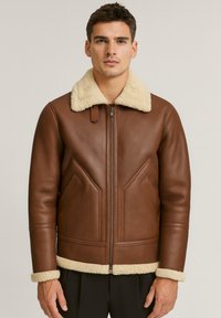 Giacca di pelle marrone con colletto e polsini in shearling crema, dotata di una zip frontale e design delle tasche in diagonale. Texture liscia.
