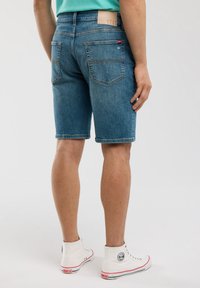 Gaiši zilie džinsi īsās bikses ar regulāru piegriezumu, piecām kabatām un kontrastējošiem šuvumiem. Valkā ar baltām augstām kedām.