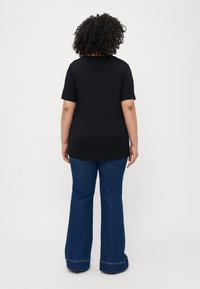 Svart t-skjorte med kort erm og avslappet passform, sammen med blå flagrende jeans med oppbrettede kanter. Glatt tekstur med minimale designdetaljer.