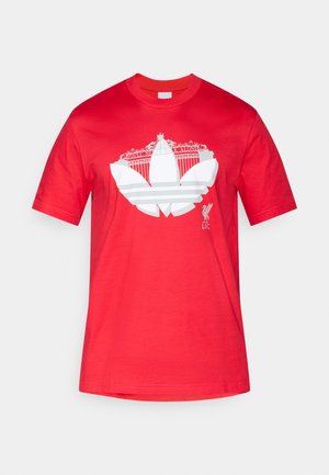 Κόκκινο βαμβακερό T-shirt με λευκό γραφικό σχεδιασμό ενός κτιρίου και το κείμενο "YOU'LL NEVER WALK ALONE," με λεπτομέρεια λογότυπου στο κάτω μέρος.