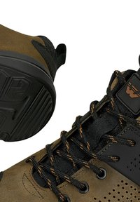 Bottes de randonnée marron et noires avec des lacets noirs et orange, une languette rembourrée et une semelle en caoutchouc texturée visible.