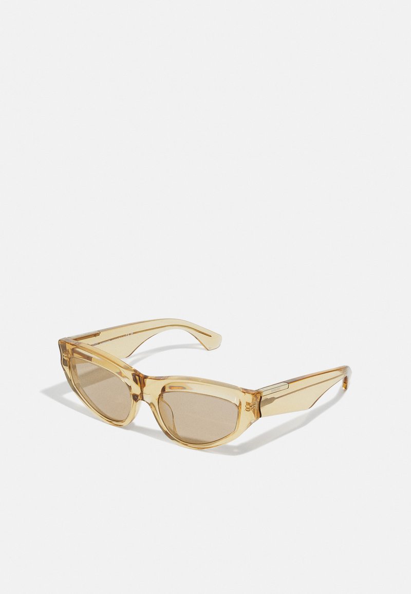 Gafas de sol ámbar translúcidas con forma de ojo de gato, lentes marrón claro y patillas gruesas con detalles de metal en las bisagras.