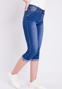 Pantalones capri de mezclilla en azul medio con un diseño ajustado, dobladillos acampanados y detalles de costura sutiles. Combinados con zapatillas blancas.