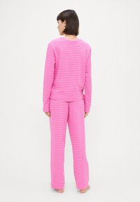 Rúžové pruhované pyžamo vyrobené z mäkkej tkaniny; dlhý rukáv s okrúhlym výstrihom a zodpovedajúce nohavice, obe so širokými bielymi pruhmi.