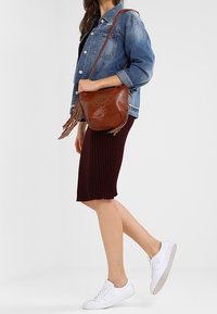 Džínová bunda, hnědá kabelka s třásněmi a kovovými detaily, vínová žebrovaná sukně a bílé tenisky. Jednoduchý a ležérní outfit.