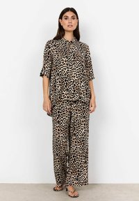 Set za udobno nošenje s leopard uzorkom izrađen od mekog materijala, koji uključuje košulju s kratkim rukavima s kopčanjem i hlače širokih nogavica; boje uključuju bež, crnu i smeđu.