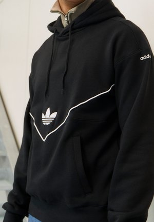 Haut à capuche noir avec un design en contour blanc, présentant un logo central. Le matériau semble doux avec une poche kangourou et un cordon de serrage ajustable.