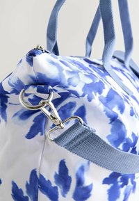 Geantă din material cu model floral albastru și alb, cu două mânere, o curea texturată pentru umăr și un clips argintiu pentru atașare.