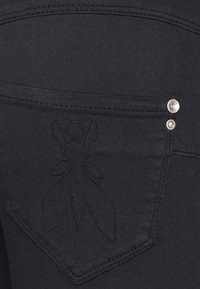 Jeans de mezclilla en un tono oscuro que cuentan con un diseño bordado único en el bolsillo trasero y remaches plateados para un detalle adicional.