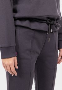 Pantaloni da tuta grigio scuro con vita regolabile con cordino, polsini a costine e tasche laterali. Realizzati in un tessuto morbido con una texture liscia.