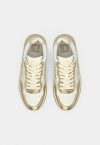 Ζευγάρι λευκά και χρυσά αθλητικά παπούτσια Veja με κορδόνια, απεικονισμένα από πάνω σε απλό λευκό φόντο.