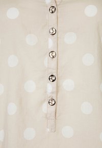 Tessuto beige chiaro con pois bianchi, caratterizzato da una patta con bottoni argentati e cuciture visibili lungo il centro.