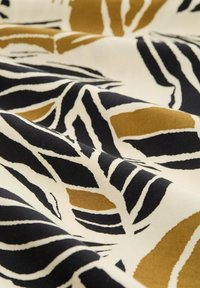 Baumwollstoff mit kräftigen schwarzen und goldenen Blattmustern auf einem cremigen Hintergrund; glatte Textur mit leichtem Glanz.