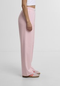 Lyserøde sweatpants med løs pasform, elastisk talje og sidesømme. Sammen med lyserøde sneakers med orange striber.