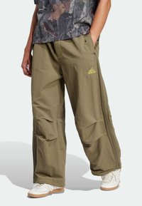 Khaki cargo pants with a lightweight material, featuring a relaxed fit, side pockets, and neon green accents, paired with white sneakers.