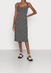 Svart ärmlös midiklänning med vitt blommönster, justerbara banden och en figursydd siluett. Vita plattformssandaler fulländar looken.