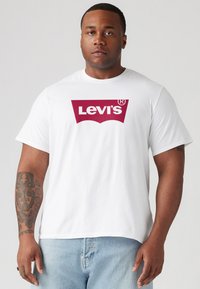White cotton t-shirt with short sleeves featuring a large burgundy Levi's logo on the front. The fit is relaxed with a crew neck design.