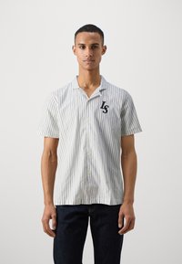 Camisa de manga corta con cuello, de rayas verticales en azul claro y blanco, que presenta un logo negro "LS" en el pecho. La tela parece ligera.