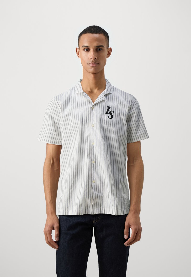 Camisa de manga corta con cuello, de rayas verticales en azul claro y blanco, que presenta un logo negro "LS" en el pecho. La tela parece ligera.